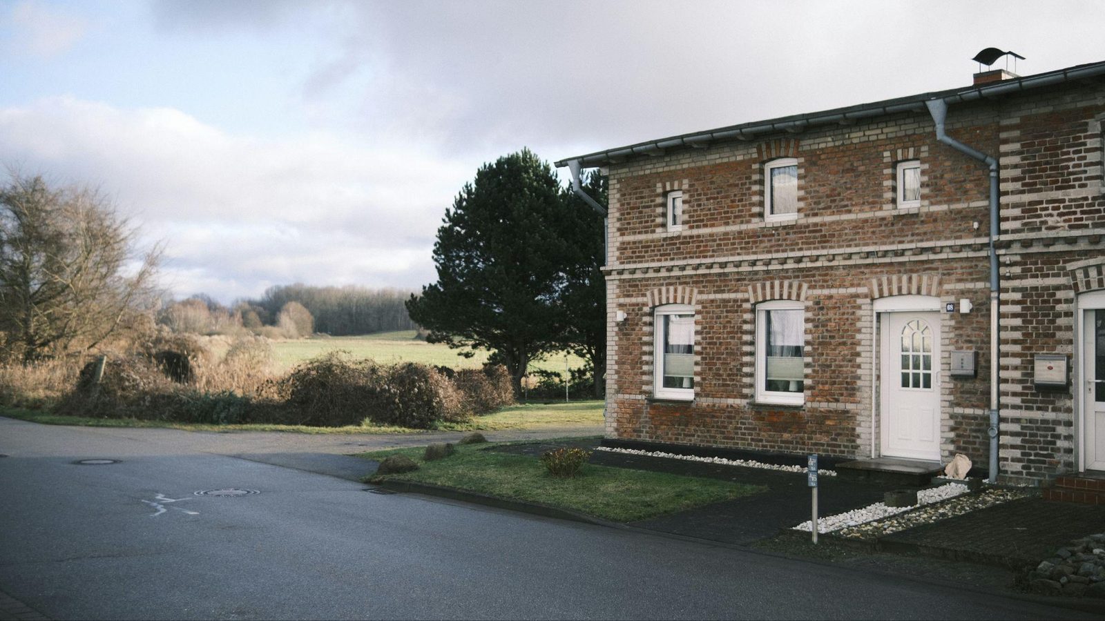 A brick home with a white front door beside a quiet road and an open grassy field